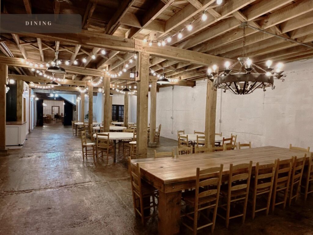 Lower-level dining hall with farm tables, string lights and chandeliers